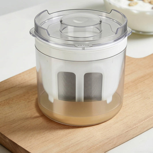 A clear plastic and white kitchen strainer or filter container with a transparent lid, shown on a wooden cutting board with a light-colored countertop in the background.